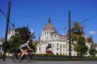 Image shows Anna cycling past the Hungarian Parliament building in Budapest (Hungary) at the start of a gravel bikepacking trip around Central Europe.