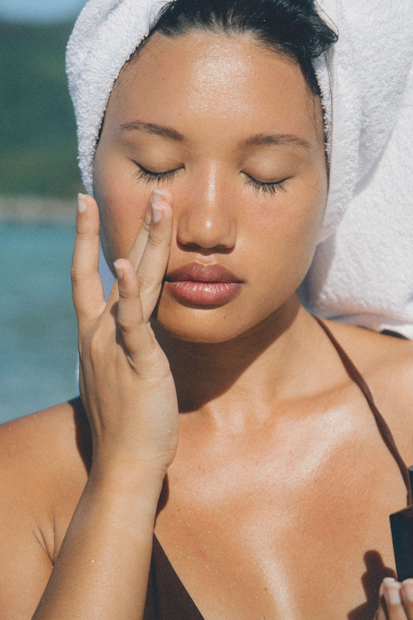 A woman wearing a towel in her hair, closing her eyes as she touches her under eye