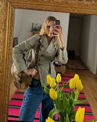 Lucia wears a pale green jacket, blue jeans, and a brown buckle shoulder bag.