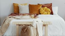 closeup of a cozy bedroom and a bed with a white comforter and red, orange and yellow velvet pillows