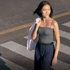 A woman wearing a vest, suit trousers, and holding a shirt over one shoulder from Uniqlo.