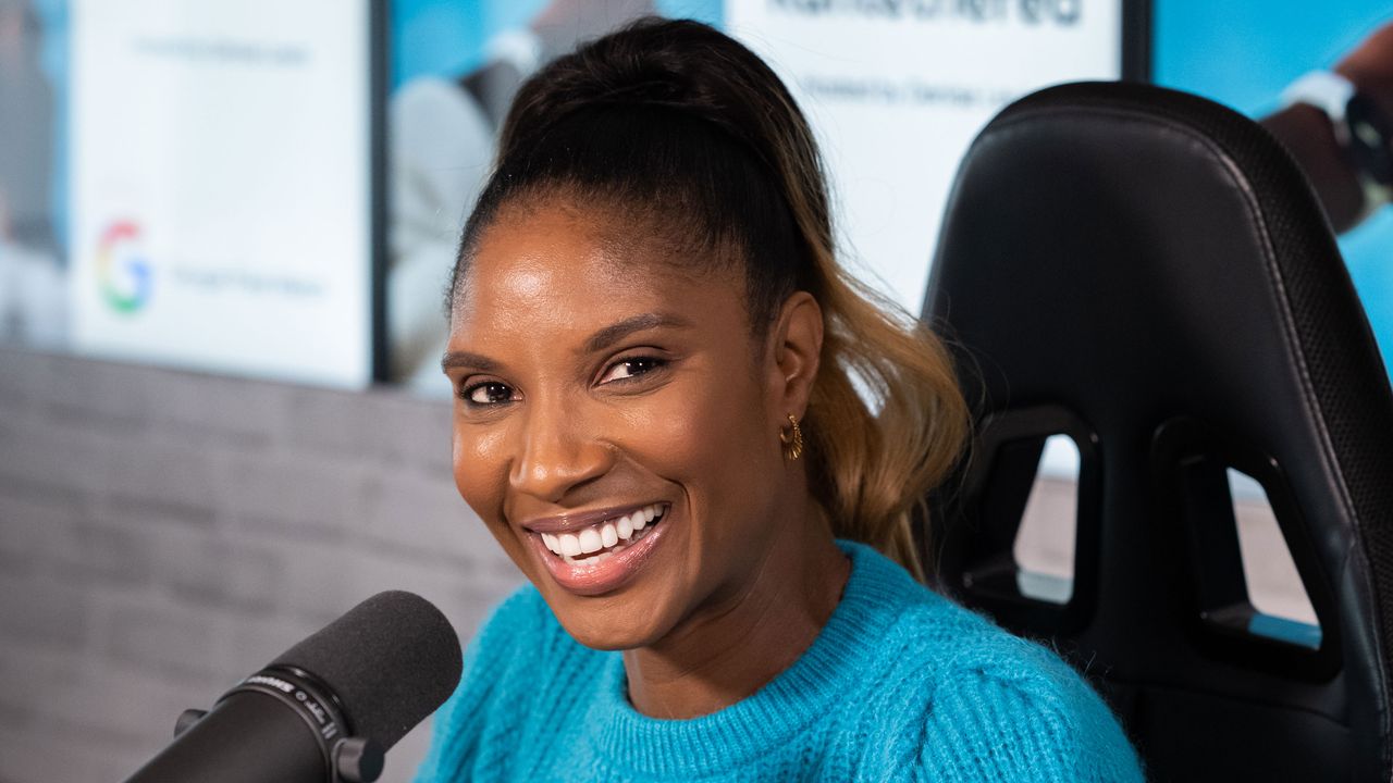 Denise Lewis in a studio wearing a blue jumper, presenting her podcast