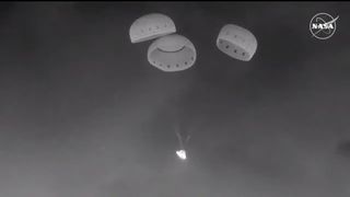 a black and white image of a cone-shaped spacecraft dangling under parachutes at night