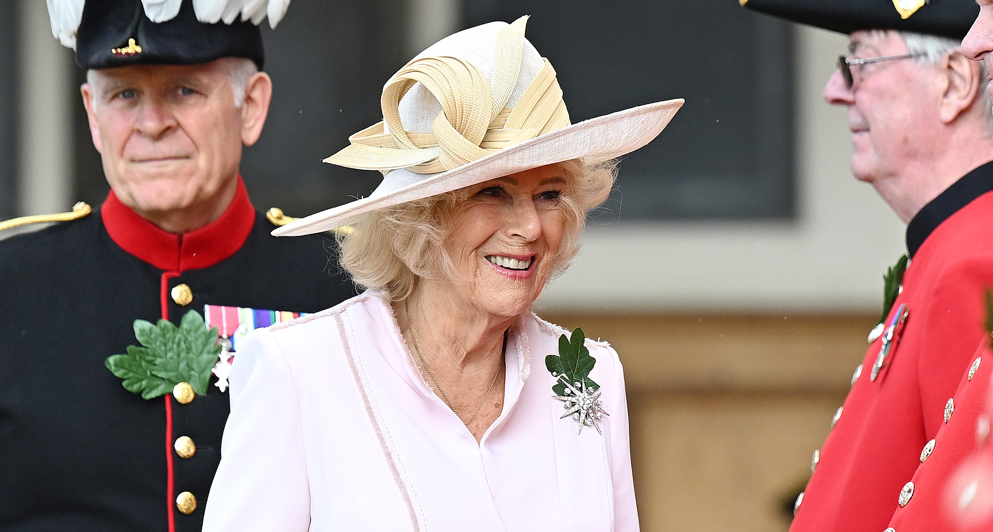 Queen Camilla wearing a pink coat and hat standing with Chelsea pensioners