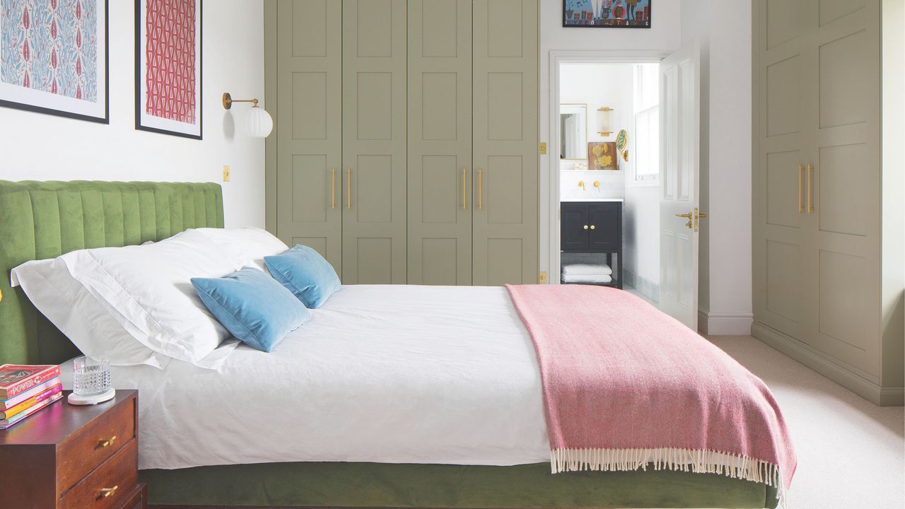 White painted bedroom with sage fitted wardrobes on two of the walls, a green bed frame and white bedding, and a door to the en-suite