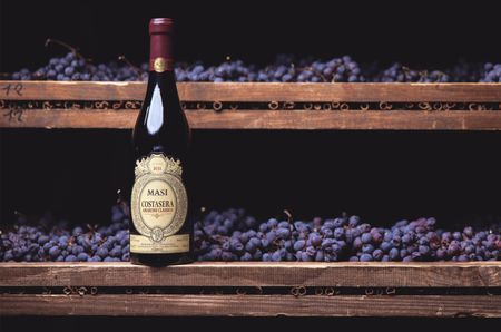 Bottle of Amarone, in front of wooden racks of black grapes