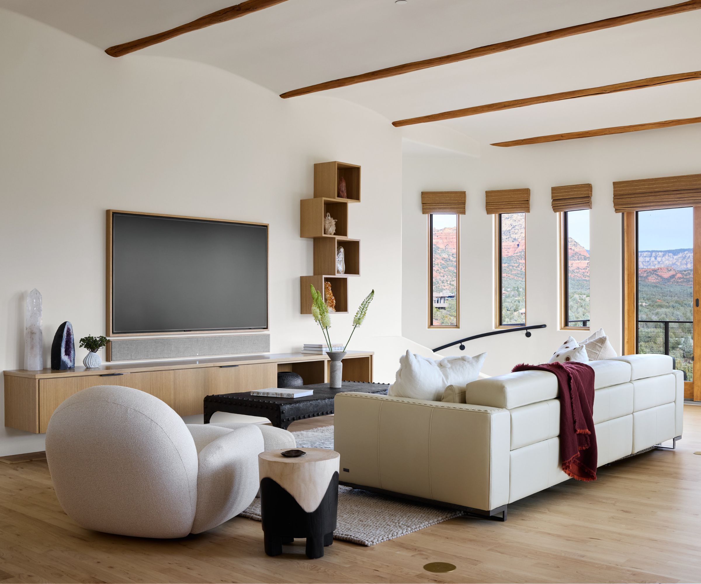 Modern minimal living room with cream sofa, curved cream armchair centered around a tv, warm wood floor, shelving and crystals surrounding