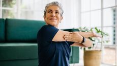 Woman doing yoga for strength work, sitting on living room floor and stretching