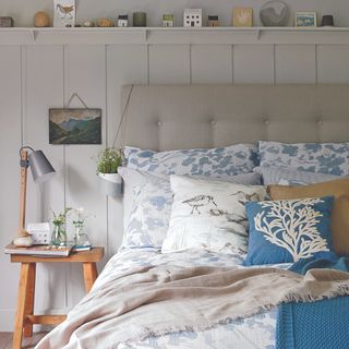 Grey bed with neutral patterned bedding and blue cushion with tree, nexy to wooden bedside table and plant