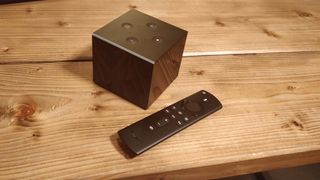 The Amazon Fire TV Cube (2nd Generation) pictured next to its remote on a wooden surface