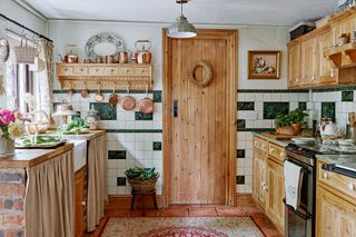 cottage kitchen with pine units and white and green tiles and curtains over shelves
