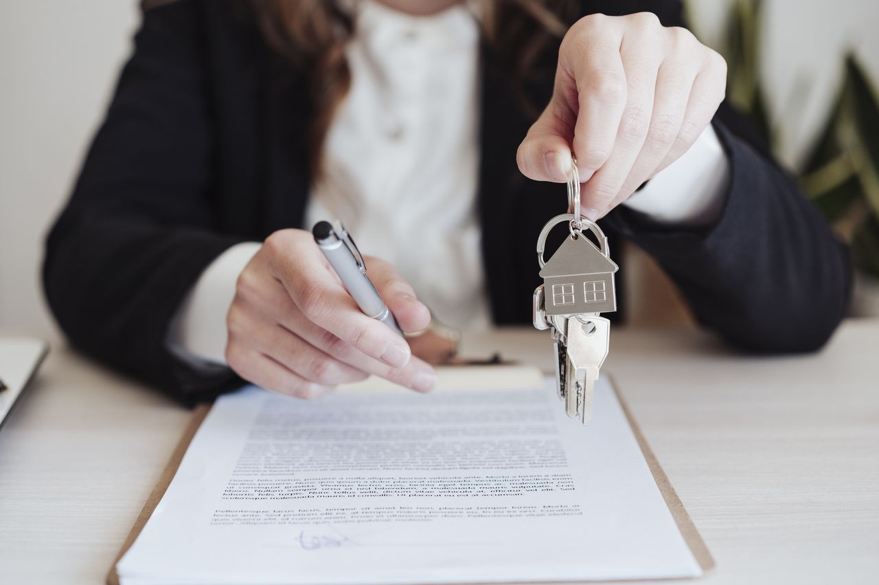 Saleswoman holding property keys and pen at office.