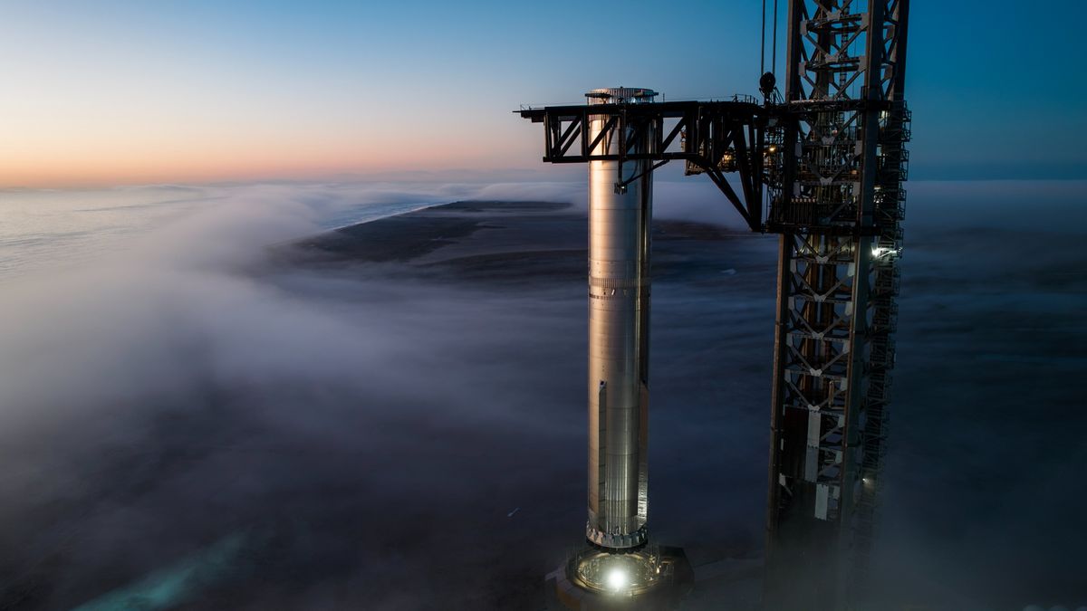 a big silver rocket is placed atop a launch pad as fog swirls around it