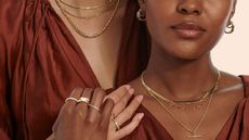 A close up of two women in burgundy, silk dresses, wearing a variety of rings, necklaces and earrings from Ernest Jones.