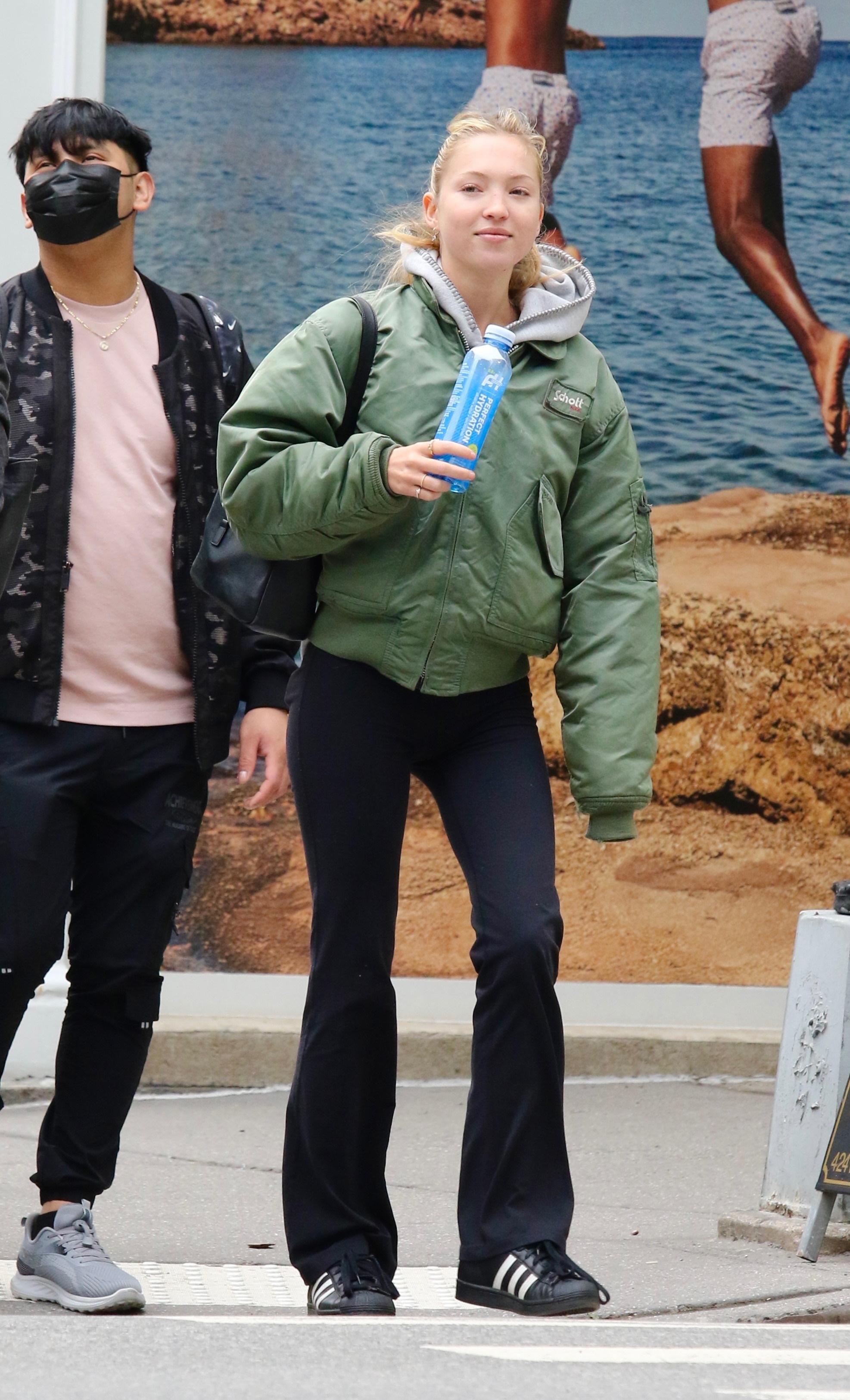 Lila Moss walks through New York Wearing Flared Leggings with black trainers and a khaki bomber jacket.