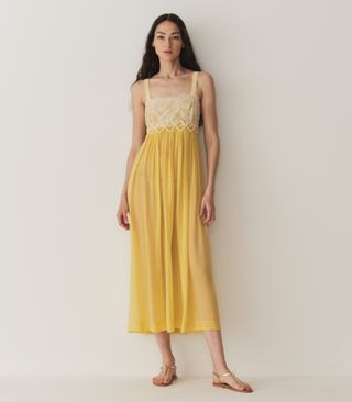 a model wears a sleeveless yellow midi dress with white lace details on the bodice