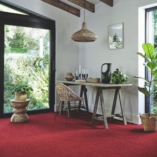study home office with a bold red carpet and a rsutci desk with wicker accessories and plants