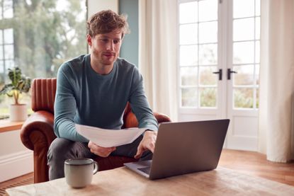 Man Sitting On Armchair At Home With Laptop Paying Bill Online