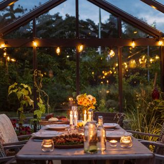 Dining table set up inside a greenhouse lit with fairylights