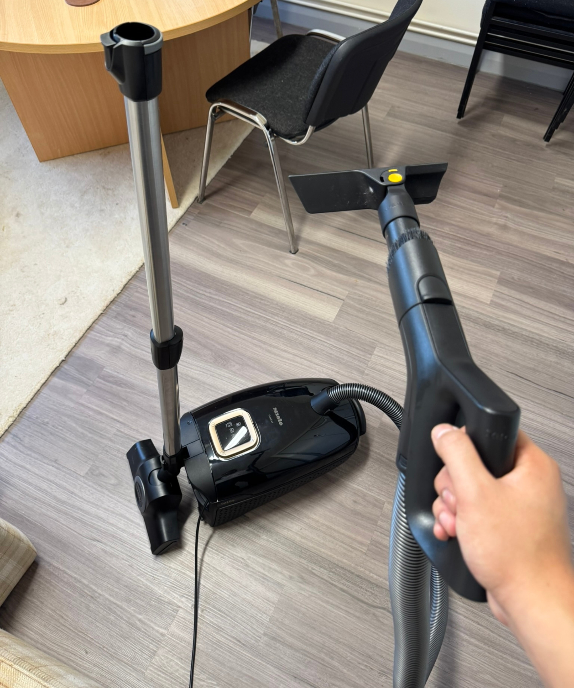 Miele Guard L1 Cat and Dog on wooden floor, with hand holding handheld upholstery attachment.