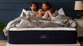 The image shows a family sitting on top of the DreamCloud Hybrid Mattress