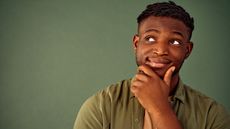 A young man looks into the distance, his hand on his chin as he wonders about something.