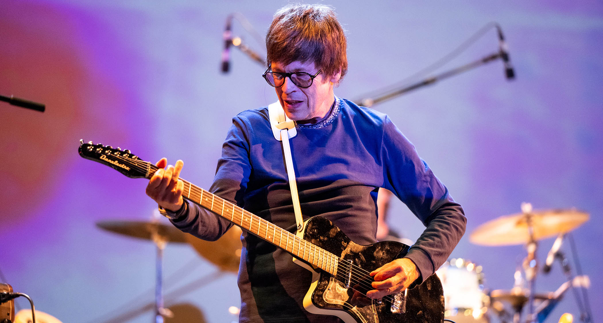 Elliott Easton of the Cars plays a black Danelectro singlecut on a stage lit in purple.