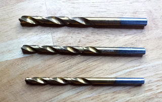 three twisted drill bits on wooden background