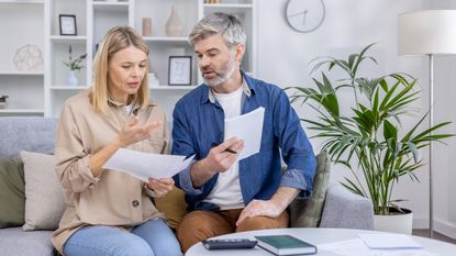 An older couple looks at paperwork together on the sofa at home.