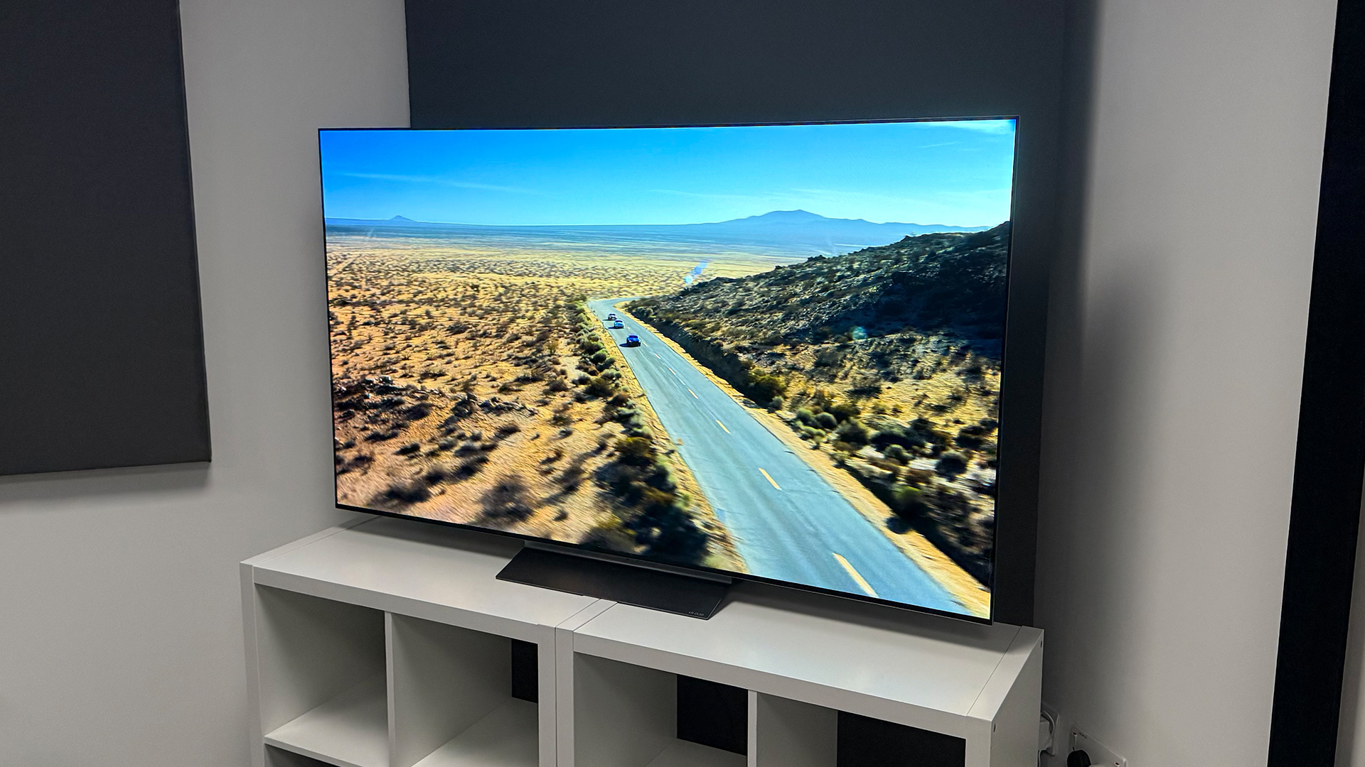 LG C6 OLED TV on white shelving unit in test room, on screen is desert road