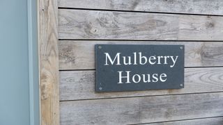 Slate house sign with white lettering on timber cladding beside front door