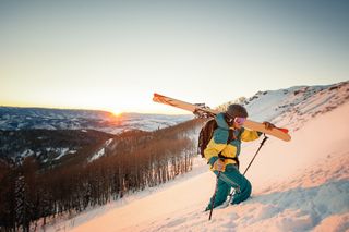 skier bootpacks with skis over shoulder