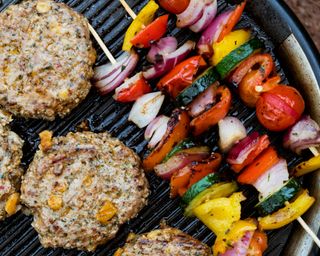 burgers and vegetable skewers on a barbecue