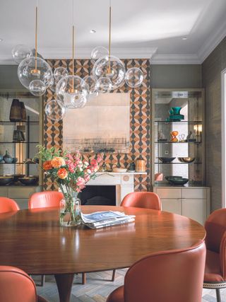 A dining room with a glass table, red chairs and a pattern wallpapered chimney breast