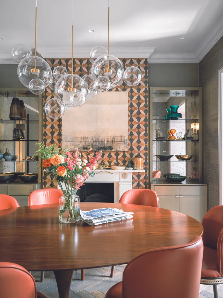 A dining room with a glass table, red chairs and a pattern wallpapered chimney breast