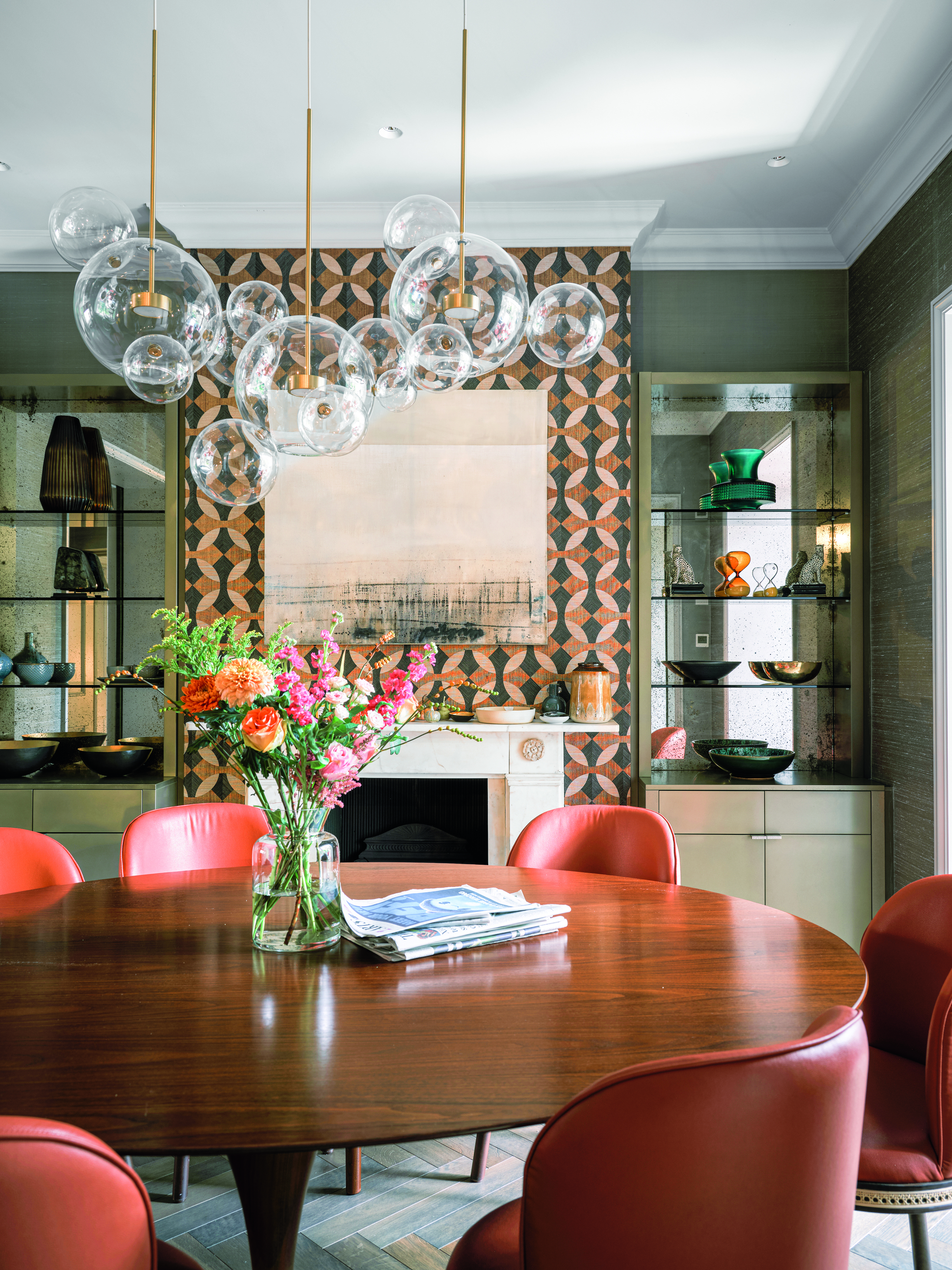 A dining room with a glass table, red chairs and a pattern wallpapered chimney breast
