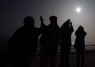 People watch with their mobile phones as clouds part to reveal the sun obscured by the moon during a partial solar eclipse at Skegness seafront in Lincolnshire, north England on March 20, 2015.