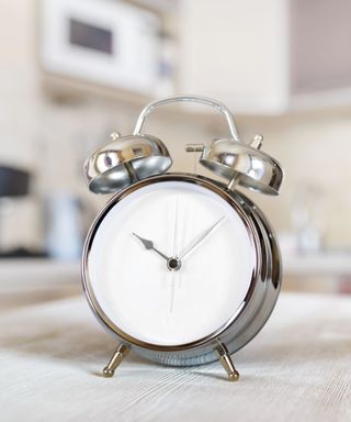 A silver clock on a countertop in a white kitchen