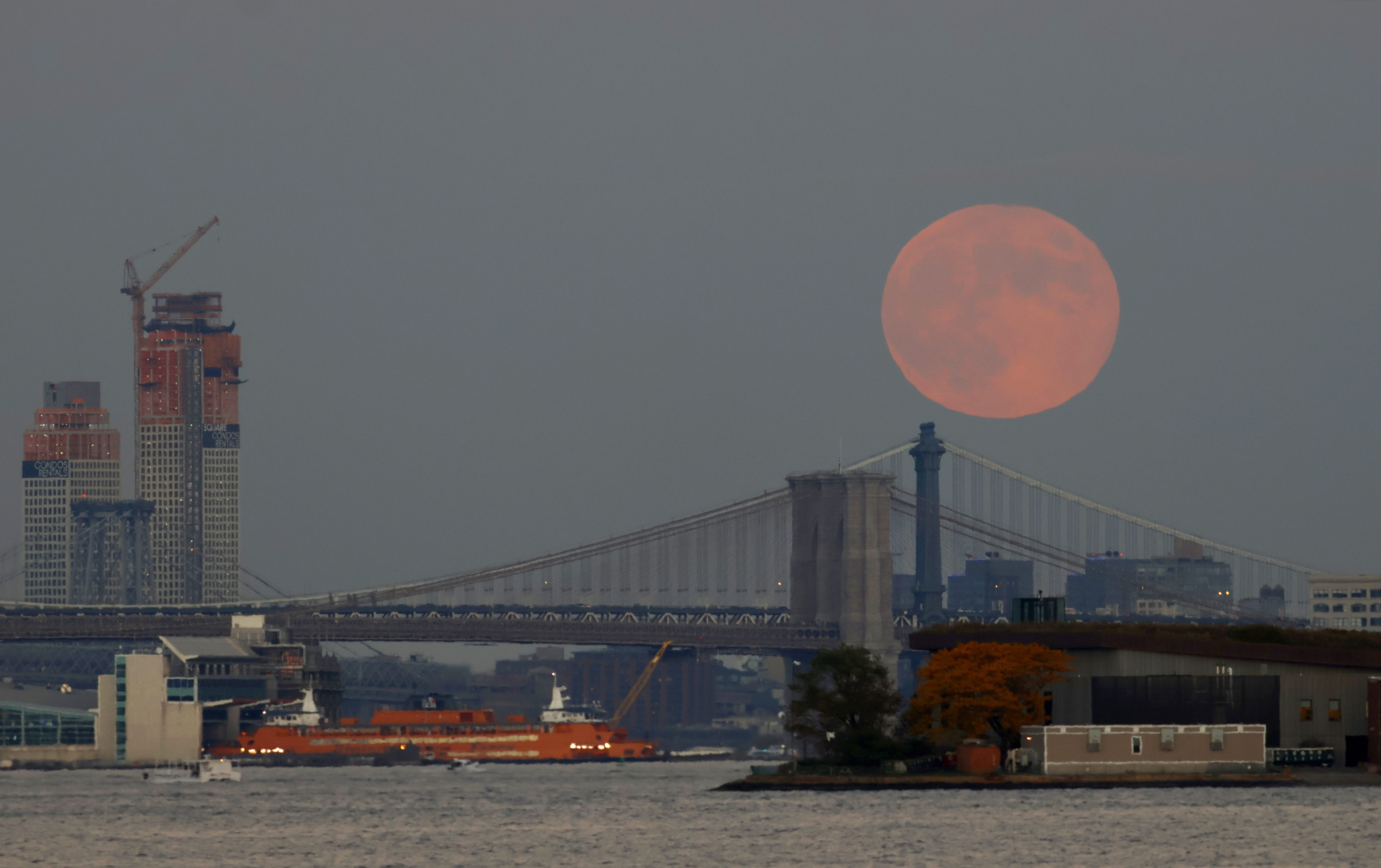 a bright full moon rises over a bridge and a city skyline