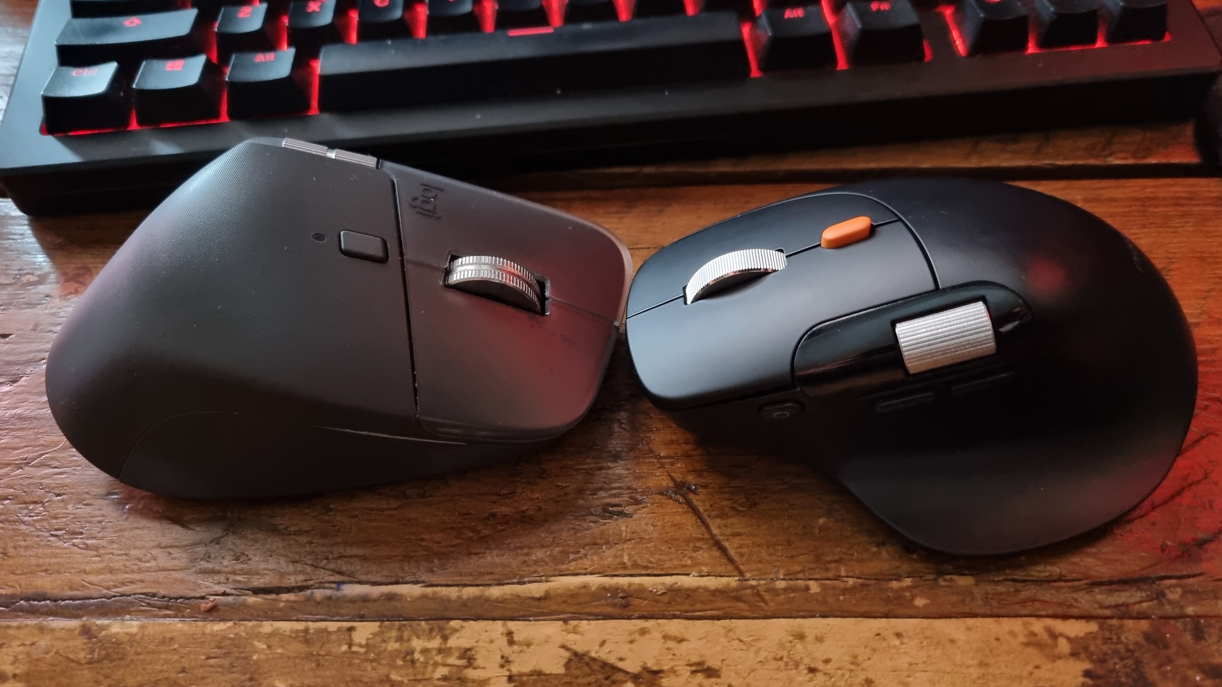 A ProtoArc EM25 ergonomic mouse facing a Logitech MX Master 4 in front of a gaming keyboard
