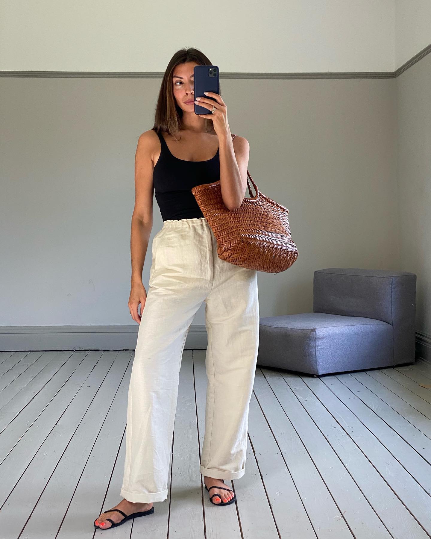 Influencer Marianne Smyth wearing a black tank top, Dragon Diffusion woven leather tote bag, pull-on white linen pants, and black strappy sandals.