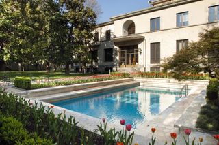 A house's swimming pool and adjacent park bath in sunlight.