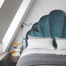 Bed with grey and white bedding and navy blue headboard, next to bedside table with books