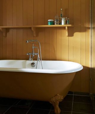 A small bathroom bathtub with shiplap, bath and overhead shelf, all painted in a mustard yellow paint color