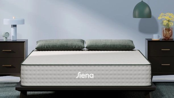 Image shows the white Siena Premier Hybrid Mattress with a dark green trim in a white-grey bedroom and decorated with green pillows