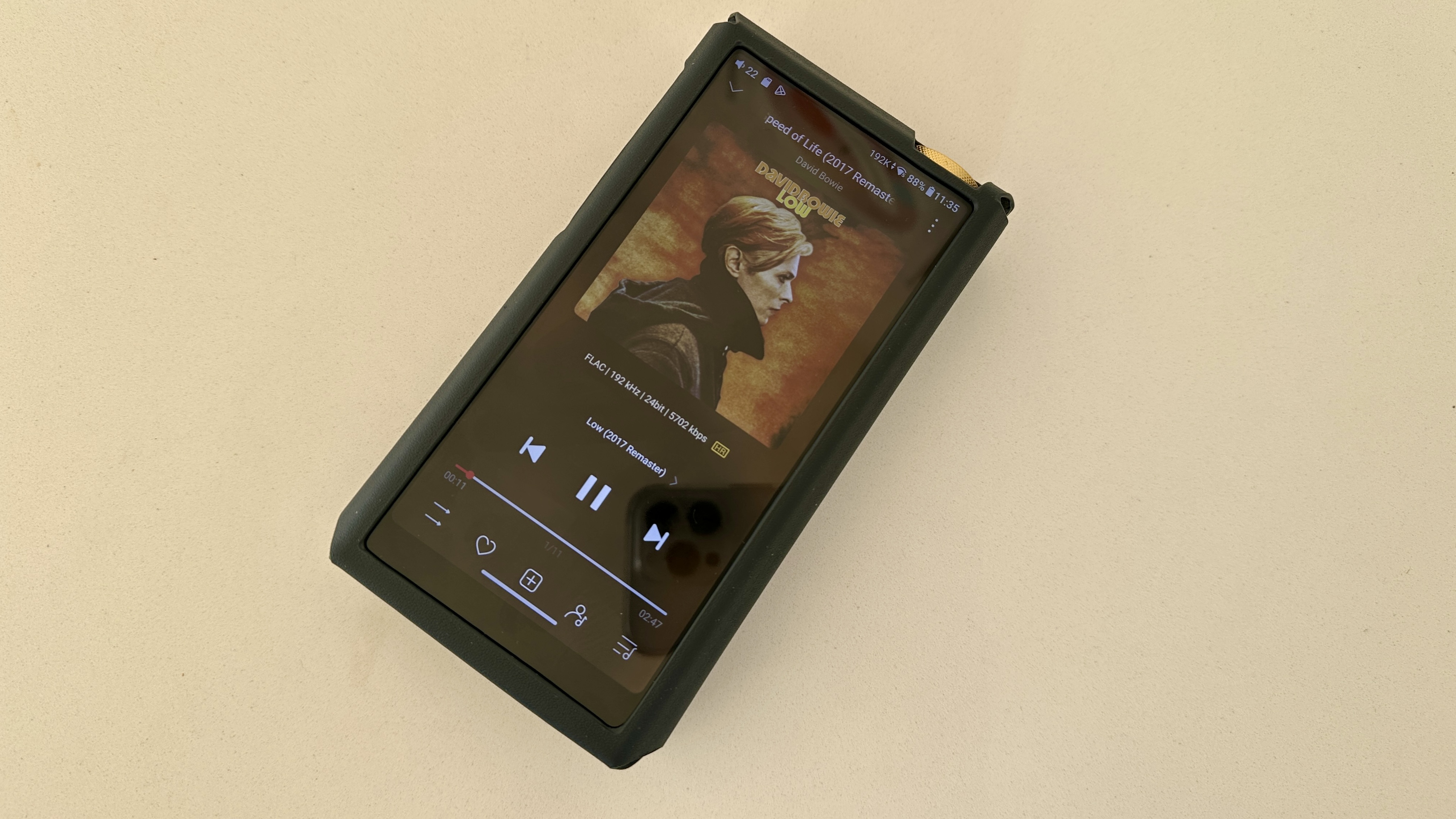 The FiiO M27 player with screen and dial showing, and content on the screen, on beige or yellow background