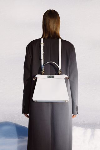 Lady stood with her back to the camera, wearing a black jacket and white bag hanging from her neck