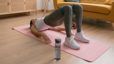 Woman doing knee exercises on a yoga mat with water bottle and resistance bands at home