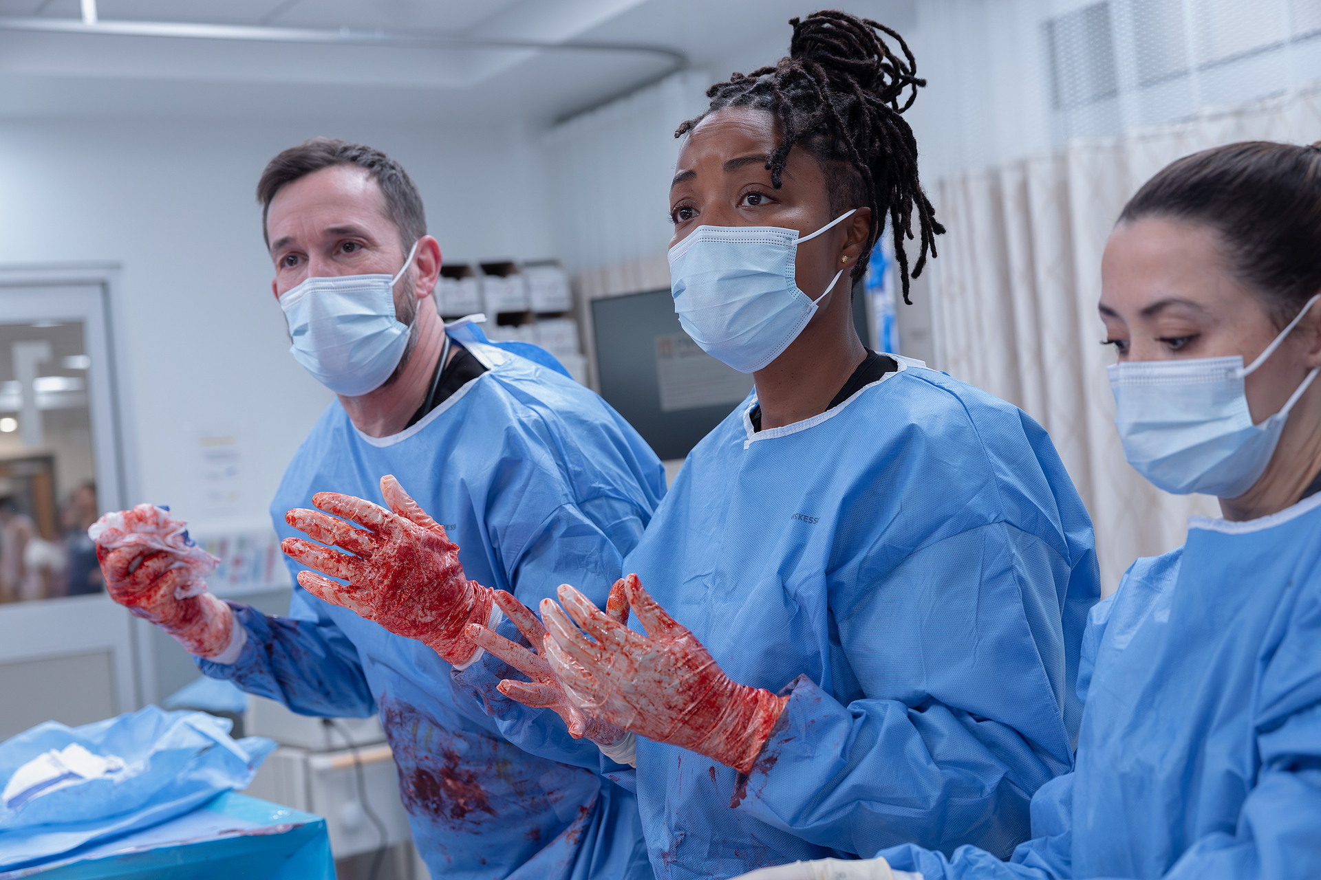 three doctors in scrubs with bloody hands played by noah wyle ayesha harris and ambar martinez perform surgery in the pitt season 2