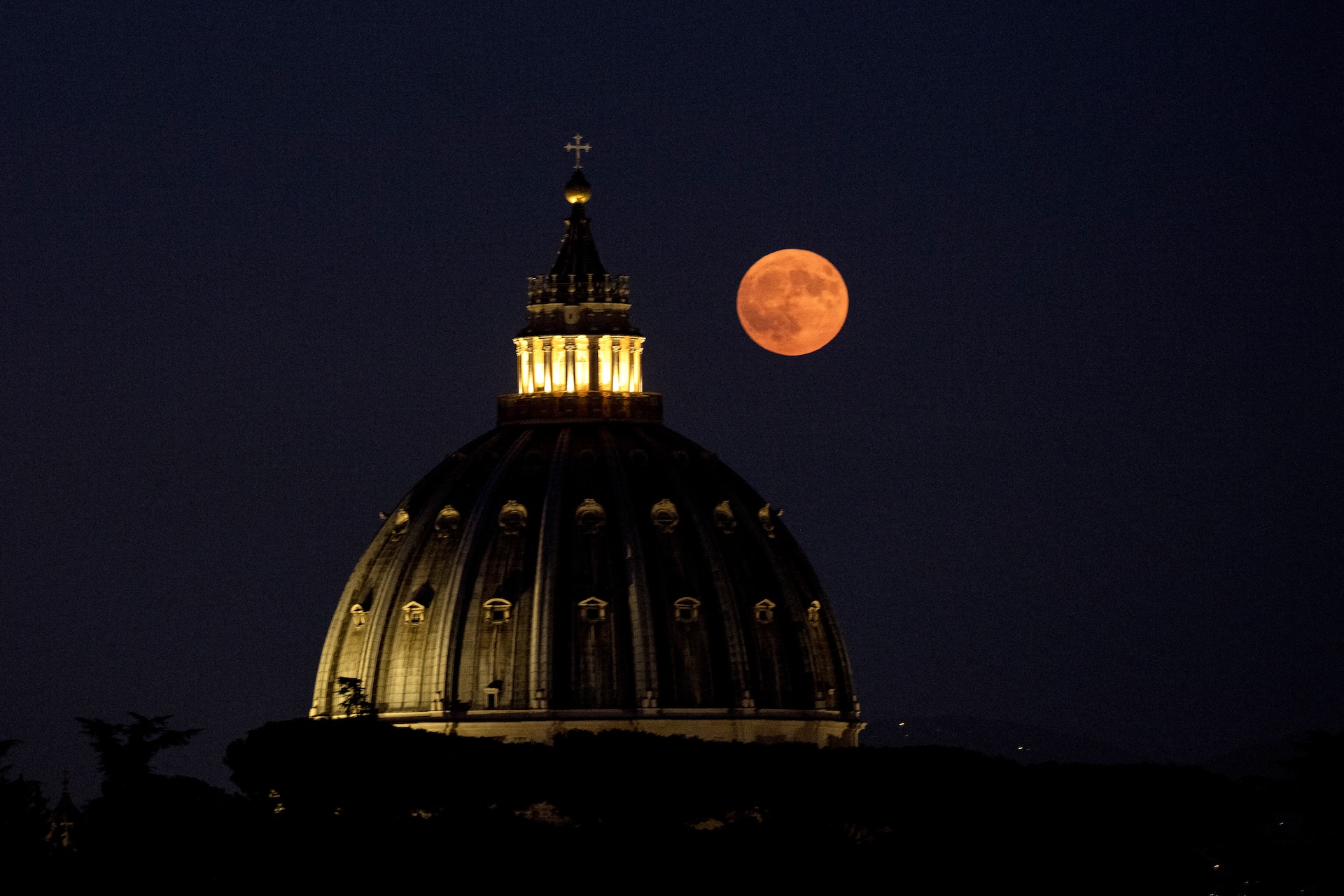 a large dome structure in the center with a large orange full moon shining directly to the right of the dome.